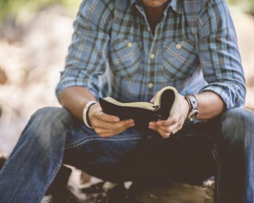 A closeup shot of a male in casual clothing reading the holy bible on a blurred background